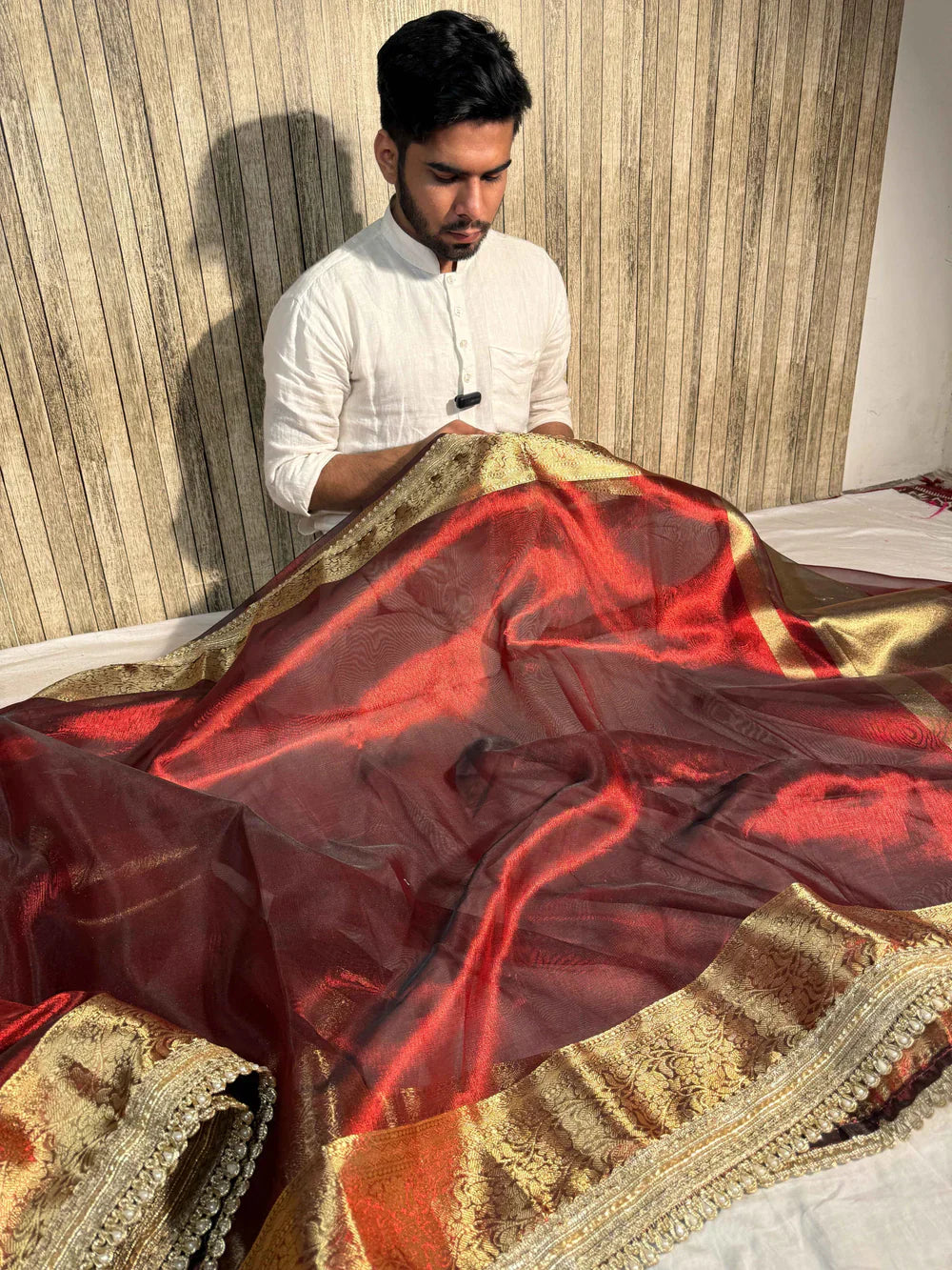 Man examining a red and gold tissue silk Banarasi saree with intricate zari border at The Surreal Store